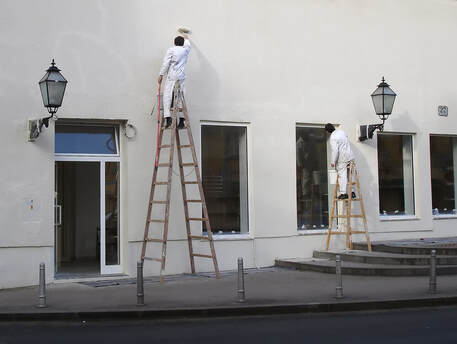 two Painters Brisbane on wooden ladders painting the side of a building with windows